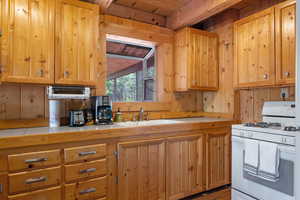 Kitchen featuring white gas range oven, wooden ceiling, wood walls, light brown cabinets, and tile countertops
