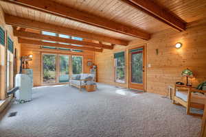 Carpeted living room featuring wooden walls and a wooden ceiling with exposed beams