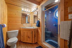 Full bathroom with wooden walls, vanity, a stall shower, and hardwood / wood-style flooring