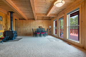 Sitting room featuring wood walls, a wood stove, carpet, and a wooden ceiling with exposed beams
