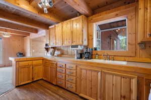 Kitchen with wooden walls, a peninsula, hardwood / wood-style floors, and a wood ceiling with exposed beams