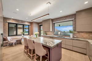 Kitchen with modern cabinets, a center island, a kitchen breakfast bar, light stone countertops, and backsplash