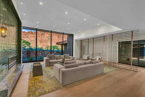 Living room with a wall of windows, a fireplace, wood finished floors, and recessed lighting