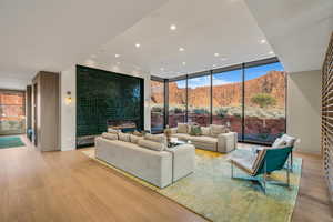 Living area with a mountain view, a tiled fireplace, floor to ceiling windows, wood finished floors, and recessed lighting