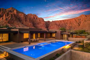 Pool at dusk with a mountain view, a pool with connected hot tub, a patio area, and an outdoor fire pit
