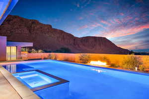 Pool at dusk featuring a pool with connected hot tub and a mountain view