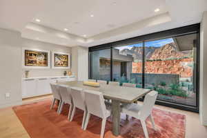 Dining space with a tray ceiling, a mountain view, light wood-style flooring, recessed lighting, and a wall of windows
