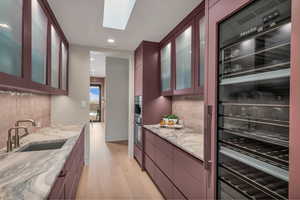 Kitchen featuring beverage cooler, light wood-style flooring, backsplash, light stone countertops, and recessed lighting