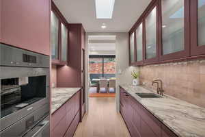 Kitchen featuring double oven, light wood-type flooring, light stone countertops, recessed lighting, and glass insert cabinets