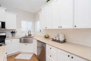 Kitchen featuring appliances with stainless steel finishes, white cabinetry, decorative backsplash, light countertops, and light wood-style floors