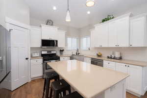 Kitchen featuring stainless steel appliances, wood finished floors, a kitchen bar, white cabinetry, and recessed lighting
