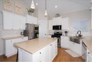 Kitchen with appliances with stainless steel finishes, backsplash, a center island, wood finished floors, and white cabinets