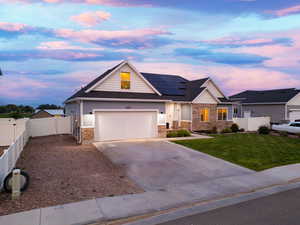 View of front of home featuring concrete driveway, roof mounted solar panels, and stone siding