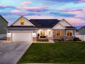 View of front of property featuring stone siding, concrete driveway, solar panels, and roof with shingles
