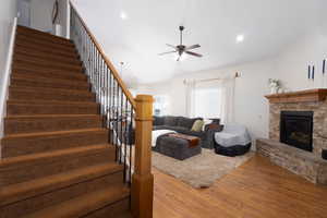 Living area with a ceiling fan, wood finished floors, stairs, and a stone fireplace