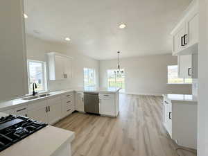 Kitchen with white cabinetry, light wood-style floors, backsplash, stainless steel dishwasher, and decorative light fixtures