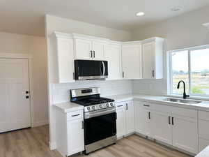 Kitchen featuring appliances with stainless steel finishes, white cabinets, light wood-style floors, decorative backsplash, and recessed lighting