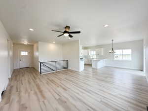 Unfurnished living room featuring light wood-style flooring, a chandelier, recessed lighting, and a ceiling fan