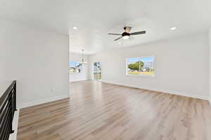 Unfurnished living room featuring a chandelier, light wood finished floors, ceiling fan, and recessed lighting