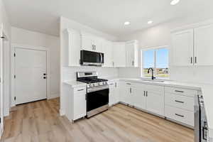 Kitchen with appliances with stainless steel finishes, light countertops, white cabinetry, light wood finished floors, and tasteful backsplash