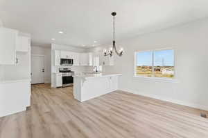 Kitchen featuring a peninsula, stainless steel appliances, light wood-type flooring, a chandelier, and recessed lighting