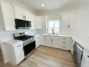 Kitchen with appliances with stainless steel finishes, white cabinetry, light wood-style flooring, and recessed lighting
