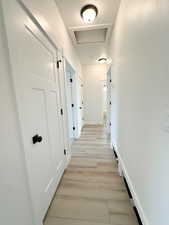 Hallway with attic access, light wood-type flooring, and a textured ceiling