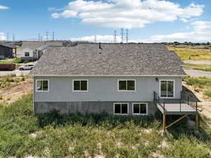 Rear view of property with roof with shingles, stucco siding, and a deck