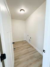 Washroom featuring a textured ceiling, light wood finished floors, and hookup for an electric dryer