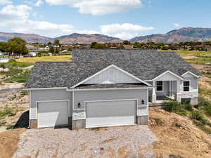 View of front of house with board and batten siding, a shingled roof, stone siding, a mountain view, and driveway