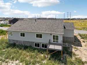 Back of house featuring roof with shingles and stucco siding