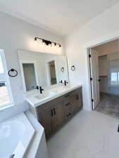 Bathroom with a walk in closet, double vanity, a bath, and light marble finish floors