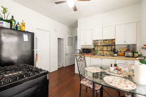 Kitchen featuring range with gas cooktop, a ceiling fan, white cabinetry, freestanding refrigerator, and dark wood finished floors