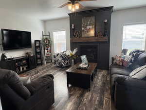 Living room with ceiling fan, dark wood-type flooring, and a large fireplace