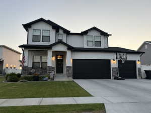 View of front of property featuring stone siding, driveway, a front lawn, board and batten siding, and an attached garage