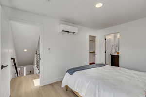 Bedroom with light wood-style flooring, recessed lighting, a wall unit AC, and connected bathroom
