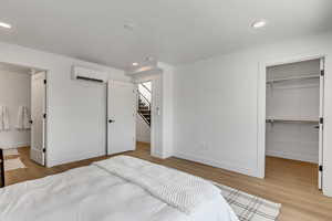 Bedroom featuring wood finished floors, a walk in closet, recessed lighting, and a wall mounted AC