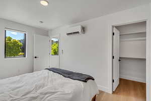 Bedroom with multiple windows, light wood-type flooring, and a wall mounted AC