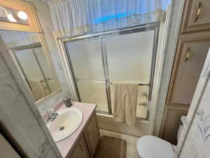 Bathroom with vanity, shower / bath combination with glass door, and wallpapered walls