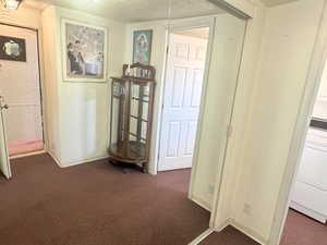 Hallway featuring dark colored carpet, washer / clothes dryer, and a textured ceiling