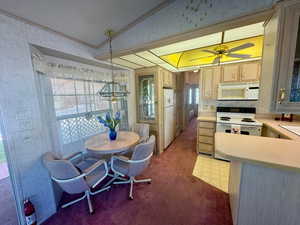 Kitchen with white appliances, vaulted ceiling, light countertops, carpet, and a chandelier