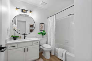 Bathroom with wood finished floors, vanity, shower / bath combination with curtain, and ornamental molding