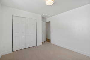 Unfurnished bedroom featuring light colored carpet, attic access, and a closet