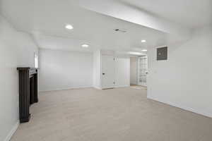 Unfurnished living room featuring light colored carpet, recessed lighting, electric panel, and a fireplace
