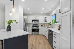 Kitchen with stainless steel appliances, light wood-type flooring, recessed lighting, white cabinets, and decorative backsplash