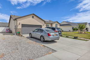 Single story home with concrete driveway, a garage, a front lawn, a residential view, and solar panels