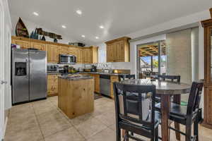 Kitchen with dark countertops, stainless steel appliances, a kitchen island, vaulted ceiling, and recessed lighting