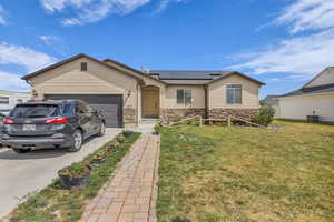 Single story home featuring solar panels, a front lawn, concrete driveway, and a garage