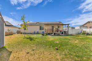 Rear view of house with solar panels, a fenced backyard, a wooden deck, and a gate