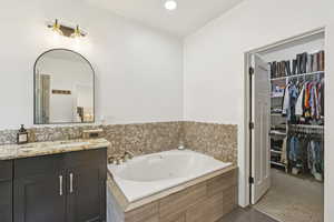 Bathroom featuring a tub with jets, vanity, a spacious closet, tile patterned flooring, and recessed lighting